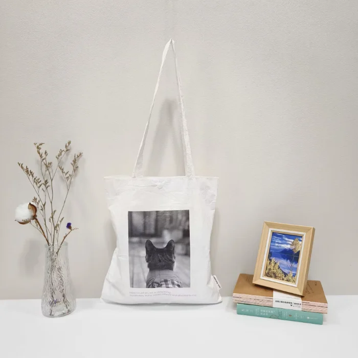 A white soft DuPont paper tote bag hanging on a hook, featuring a dog illustrat