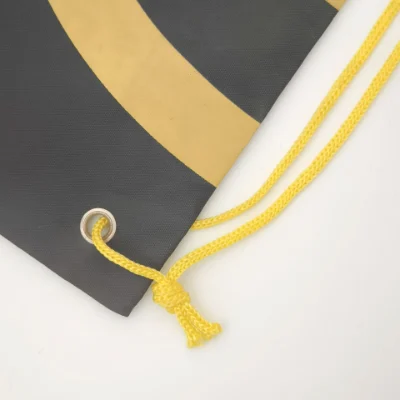 Detailed view of the bottom corner of a black and yellow drawstring backpack with metal grommet and yellow cord, customizable in size, material, style, and printing.