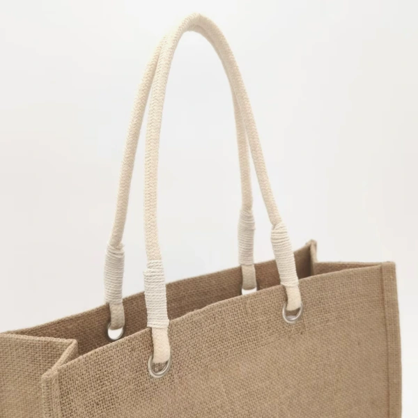 Close-up of white cotton rope handles with metal grommets on a natural jute tote bag, customizable in size, material, style, and printing.