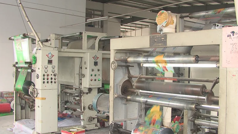 Top view close-up of gravure printing machine applying colorful ink patterns on laminated film surface, customizable in size, material, style, and printing.