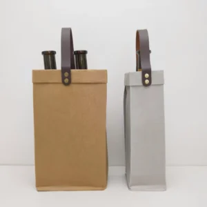 Front view of two washable kraft paper wine bags, one brown and one gray, each with a dark brown leather handle and brass - colored studs, holding wine bottles.