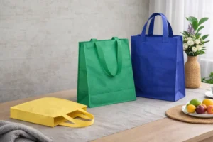 Three non-woven bags in green, blue, and yellow are displayed on a table, showing flat and upright positions to illustrate how to measure a non-woven bag.