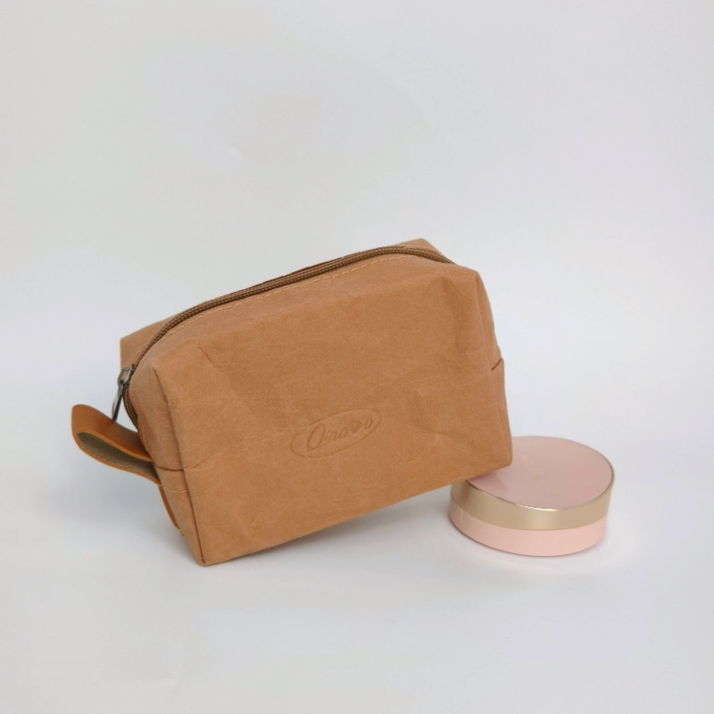 A small washable kraft zipper pouch resting on a flat surface beside two round objects against a neutral background.
