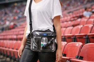 A person wearing a clear crossbody bag at a stadium with visible personal items inside, illustrating crossbody bags allowed in stadiums.