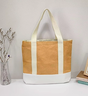 A laminated Tyvek tote bag with a structured rectangular shape, featuring contrasting handles and a reinforced base, displayed on a shelf in a simple indoor setting.
