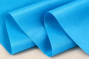 A close-up view of folded blue polyester fabric with a fine textured surface, illustrating what is polyester fabric and why is it used for reusable shopping bags.