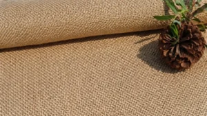 A close-up of natural burlap fabric with a pine cone, illustrating What Are Burlap Bags.