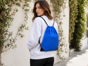 Why Custom Printed Drawstring Backpacks Are Perfect Promotional Giveaways showing a blue drawstring backpack worn outdoors with shoulder cords.