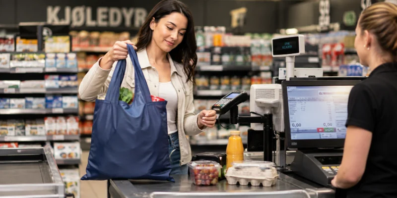 How to Use a Foldable Bag More Efficiently? A person uses a blue foldable shopping bag at a checkout counter with groceries nearby.