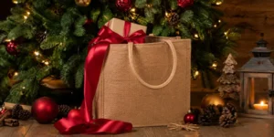 A jute gift bag with a wrapped present is placed in a Christmas decorated setting for holiday packaging.