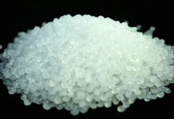 Close-up view of translucent polypropylene resin pellets piled against a dark background, used in PP woven fabric production.